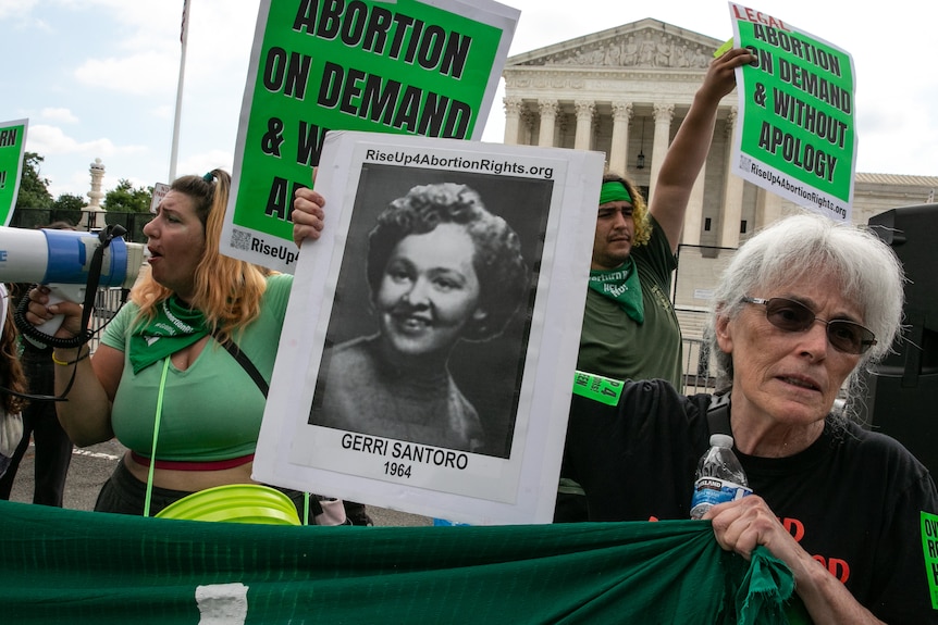 A woman with grey hair holds a black and white photo of Gerri Santoro outside the US Supreme Court