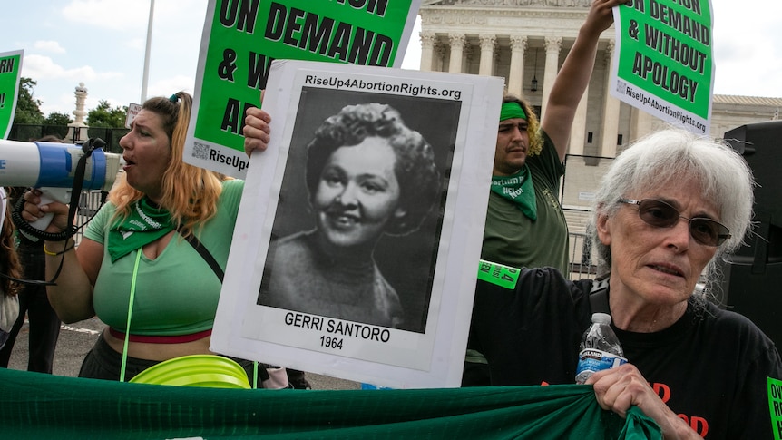 A woman with grey hair holds a black and white photo of Gerri Santoro outside the US Supreme Court