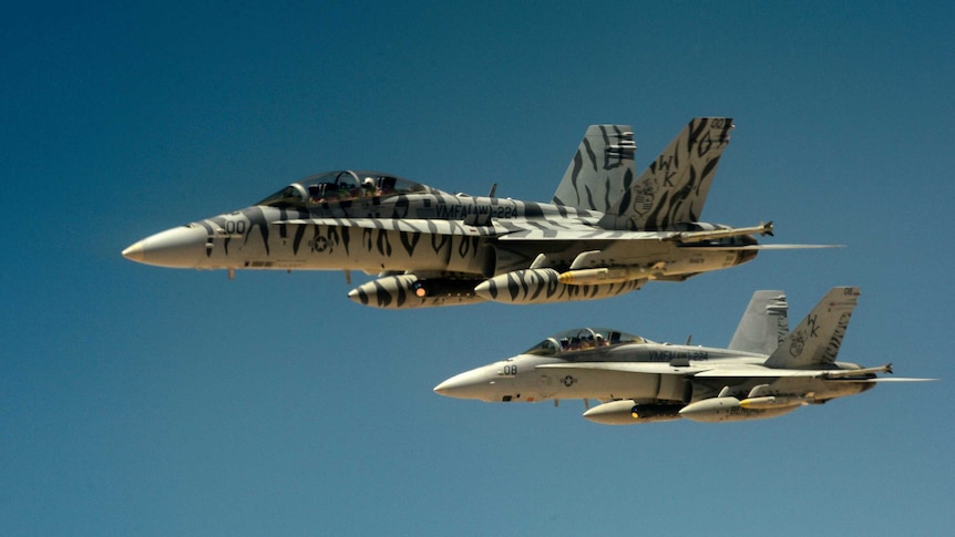 Two US Marine Corps F-18 Super Hornets fly through blue skies.