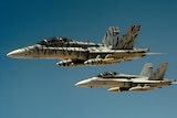 Two US Marine Corps F-18 Super Hornets fly through blue skies.