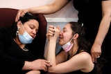 Three women hugging and crying in face masks
