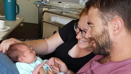 A man and woman look at a baby in a hospital room