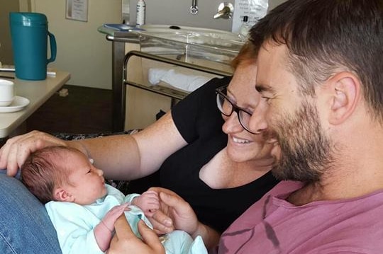 A man and woman look at a baby in a hospital room