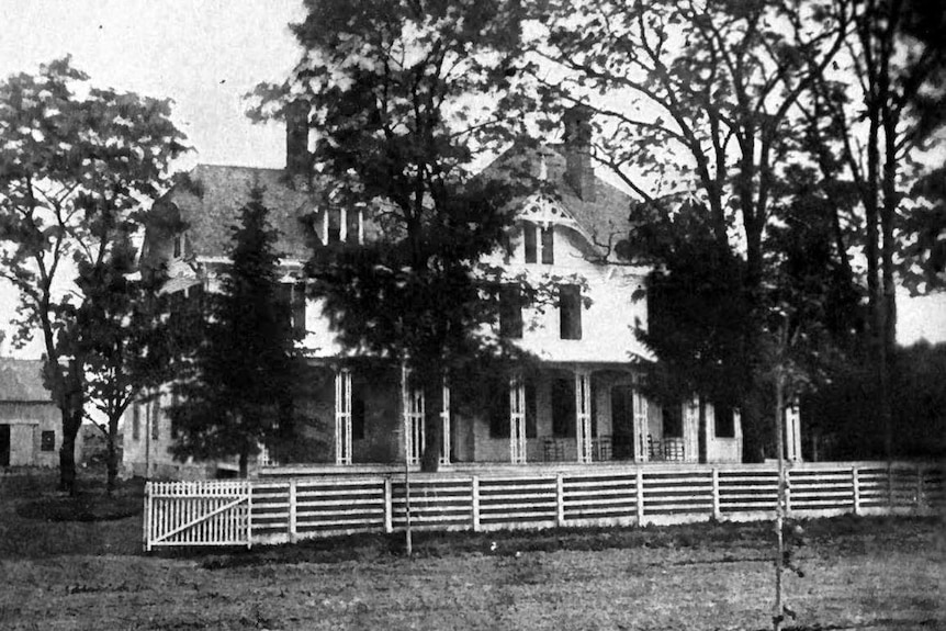 A black and white photo of a house surrounded by a fence