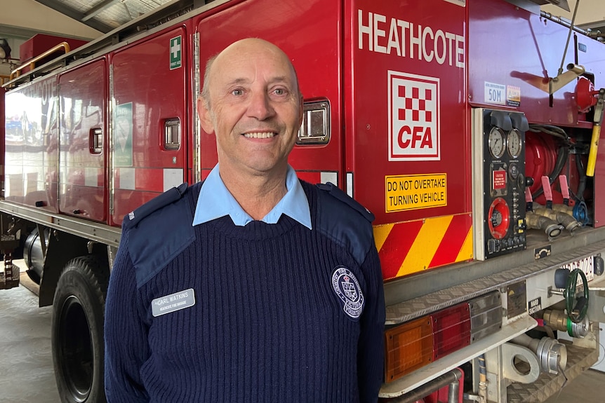 A man smiling at the camera, standing infront of a fire truck. 
