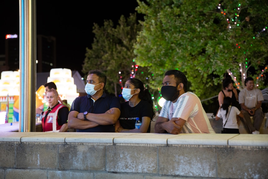 Three men wearing masks lean on a while watching NYE celebrations