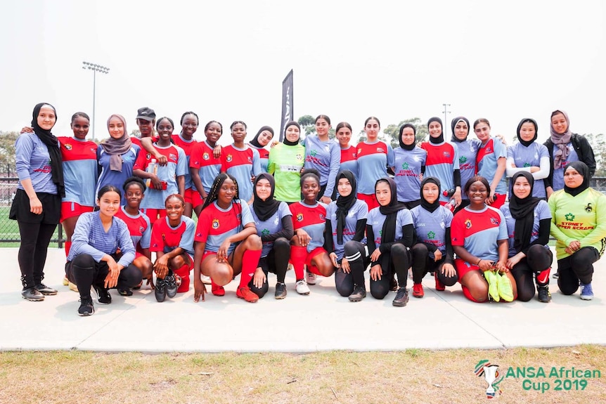 Two girls football teams stand arm in arm.