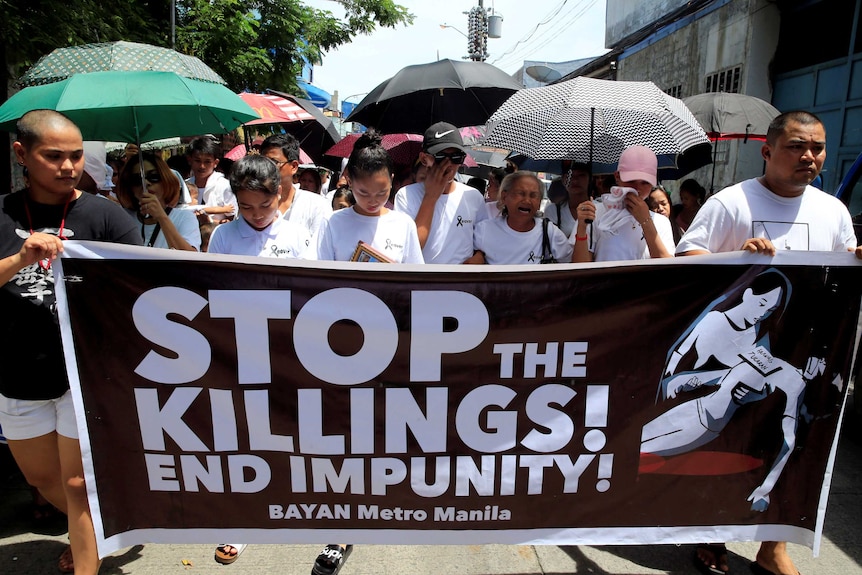 Protesters hold up a banner calling to stop the continuing rise of killings.