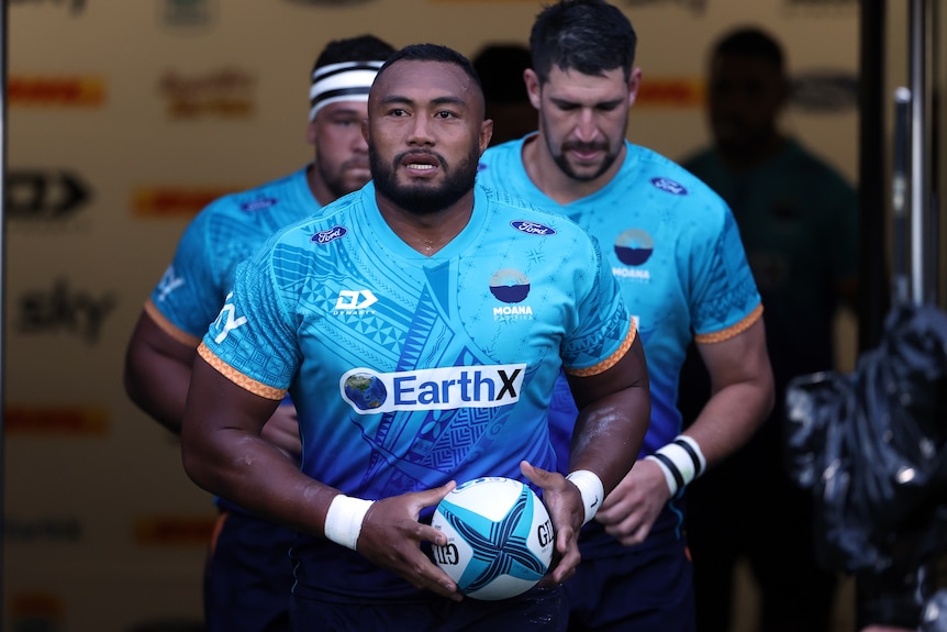 The captain of a rugby union team looks out onto the field holding a ball as he gets ready to run out. 