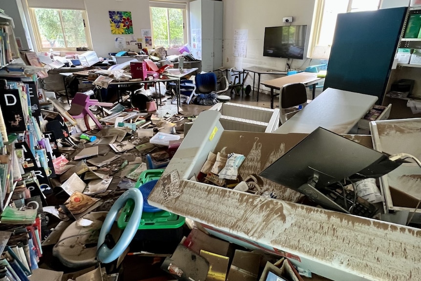 A badly damaged classroom with furniture overturned and water on the ground.