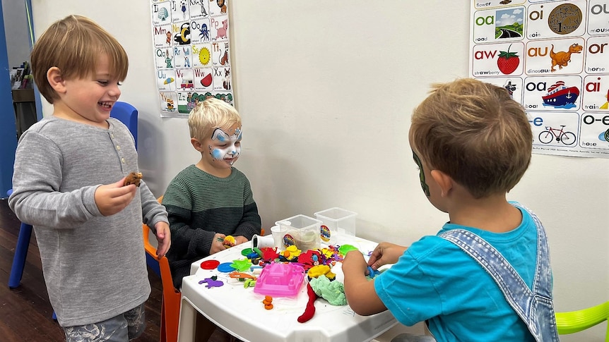 Three young boys playing togerther at a table with craft items.