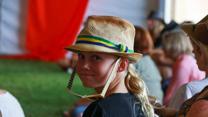 A young girl in the audience wearing a trilby and sunglasses