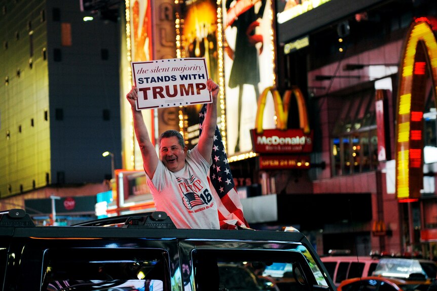A man holding a Donald Trump sign leans out of a Hummer in New York.