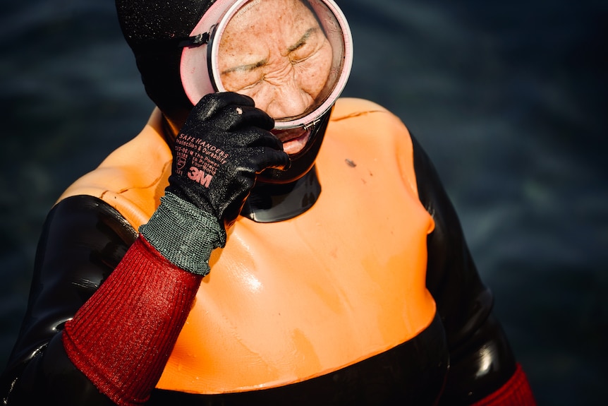 A haenyeo member wearing an orange diving vest adjusts her mask.