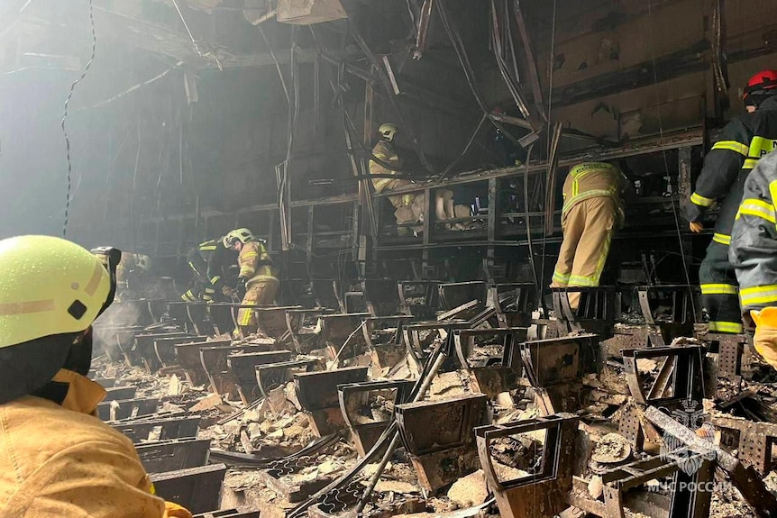 Rescue workers in high viz comb through charred remains of seats and metal in a concert hall
