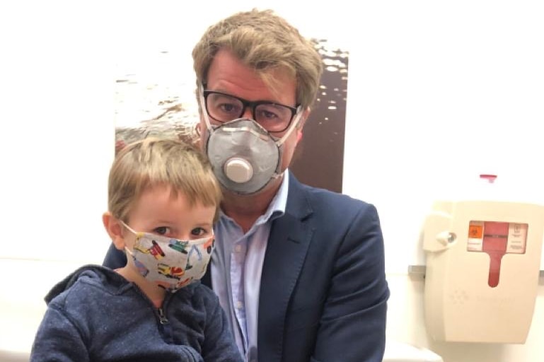 Lipson with son sitting on lap in doctor's room with both wearing masks.