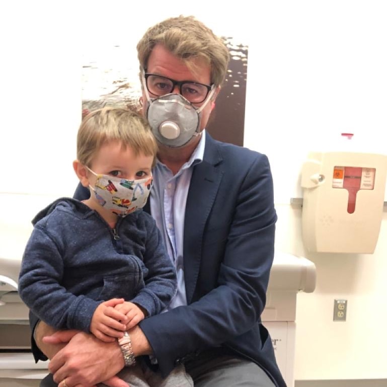 Lipson with son sitting on lap in doctor's room with both wearing masks.