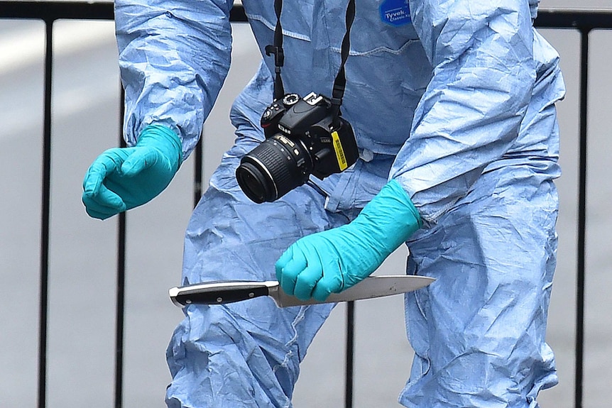 A forensic police officer wearing gloves picks up a knife.