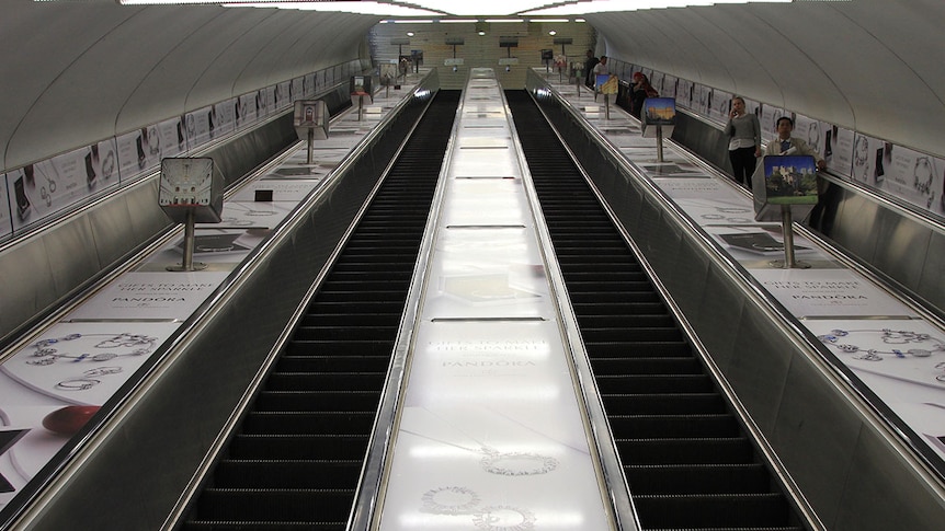Four very steep escalators in a bright, metallic tunnel.