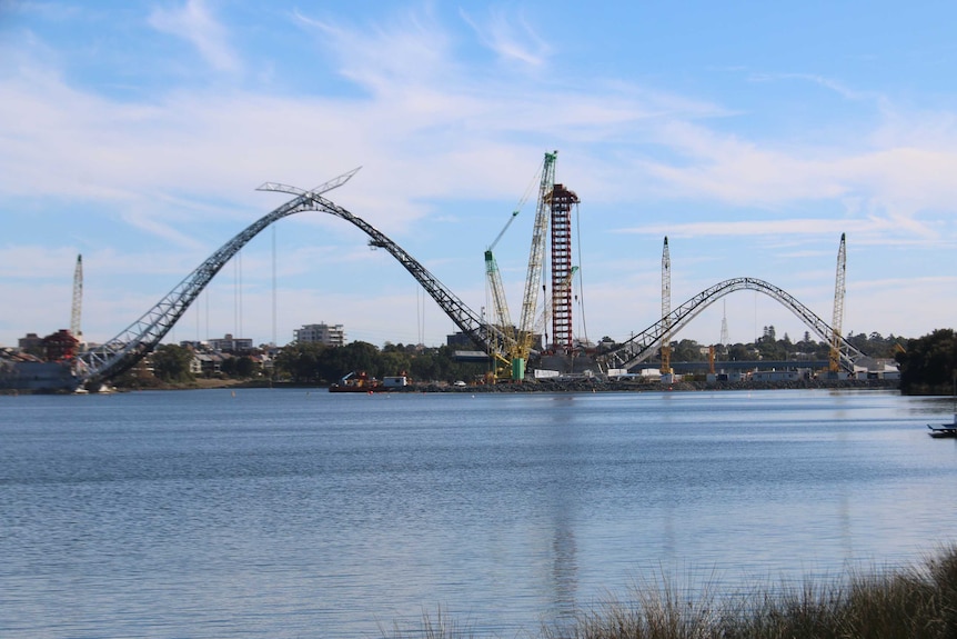 A wide, long-distance shot of the Perth Stadium footbridge under construction across the Swan River.