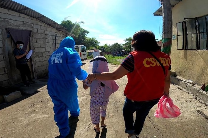 A child wearing a head covering is led away by police on dirt road.