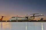 Image of a passenger prop-plane sitting outside an airport hangar.
