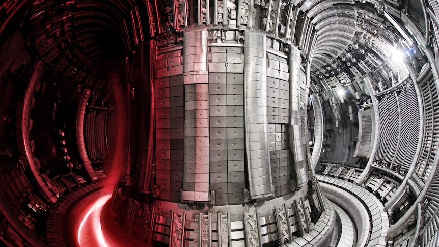 The interior of a large, silver, donut-shaped device, with dark red plasma swirling around one side.