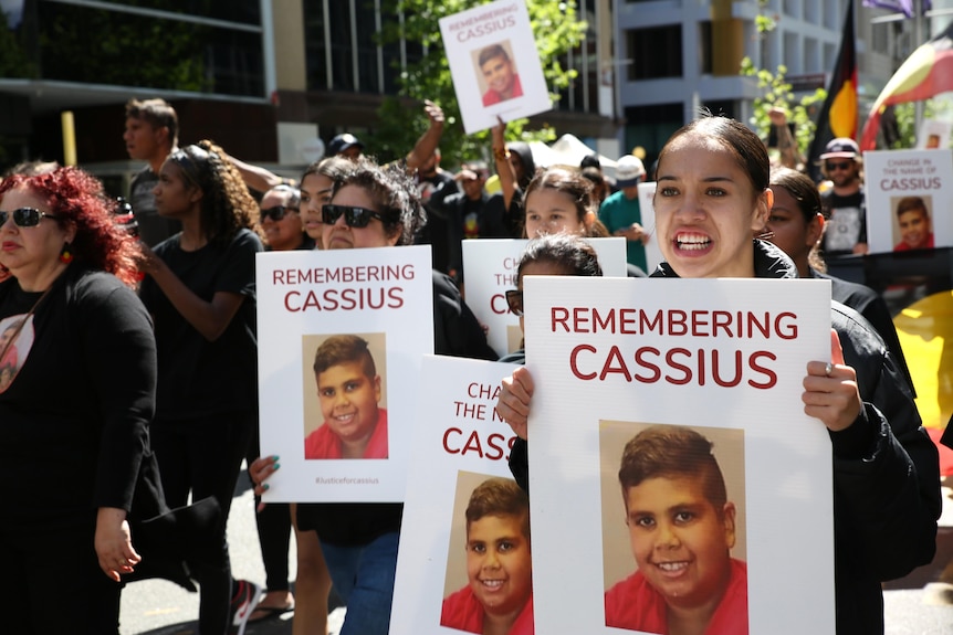 A crowd of people chanting while holding placards on the street.