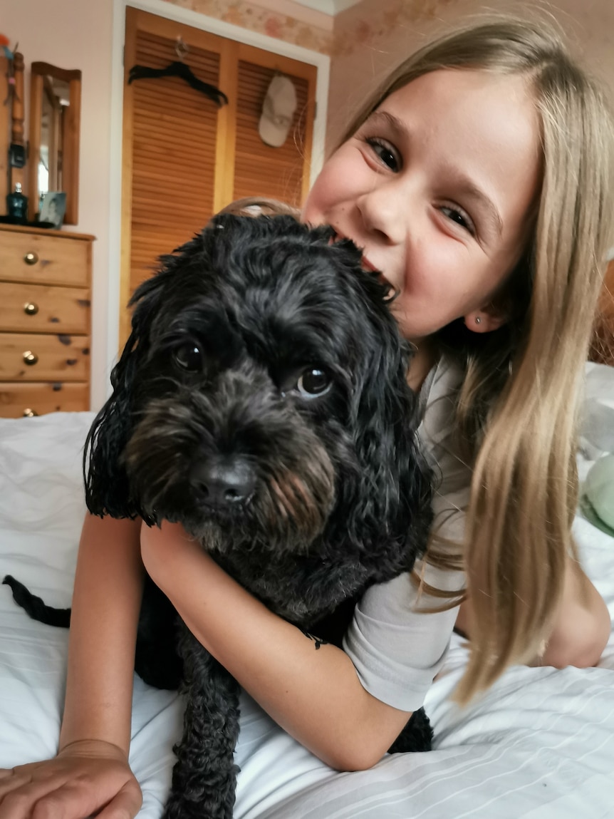 Young girl with long hair holding on to a black fluffy dog