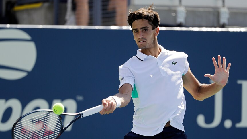 A male tennis player in a white polo shirt hits a forehand