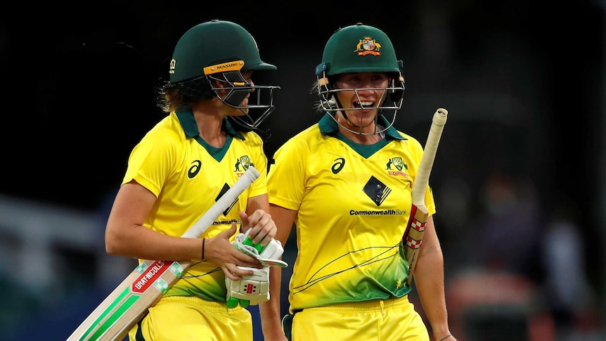 Jess Jonassen looks at Beth Mooney, who smiles as the pair walk off the field with their cricket bats under their arms.