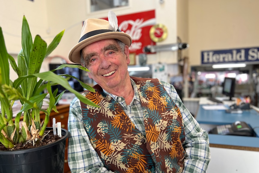 An older man wearing a jaunty hat and smiling widely inside an antique market.