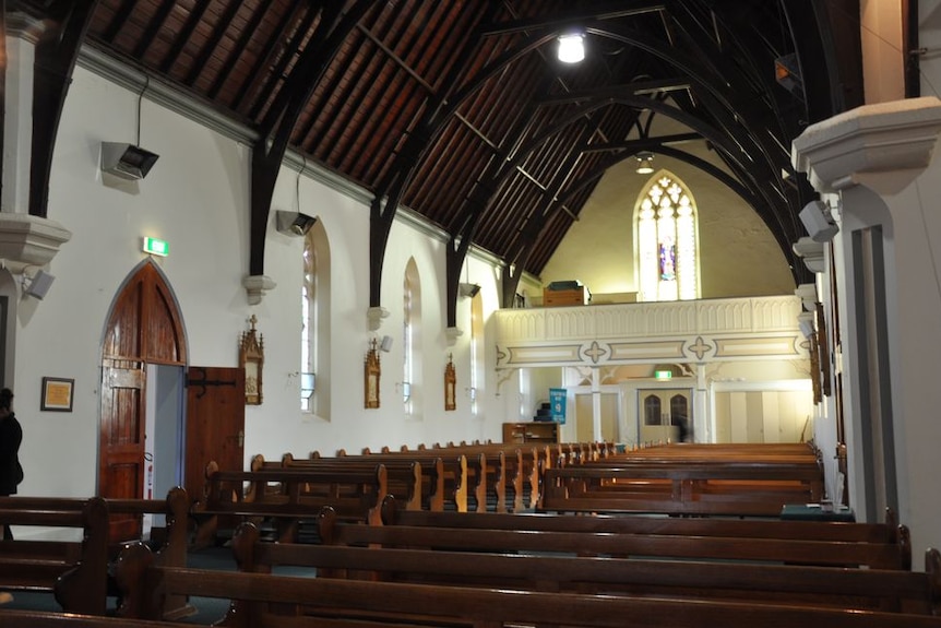 Inside a simple Catholic church with white walls and wooden pews