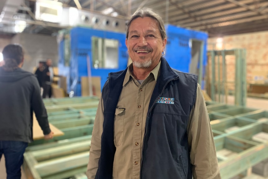 Entrenador de carpintería sonriendo frente a la construcción de madera