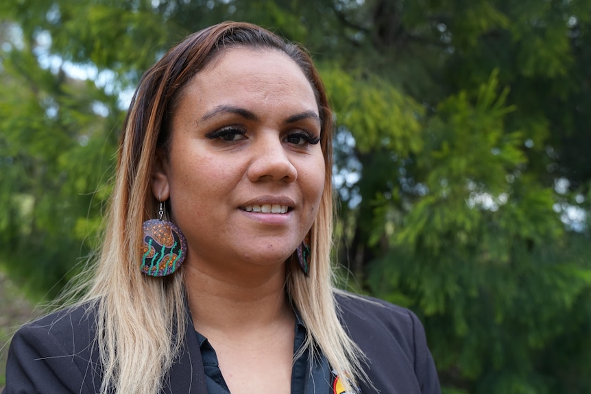 An aboriginal woman smiling to the camera with green shrubs in the background