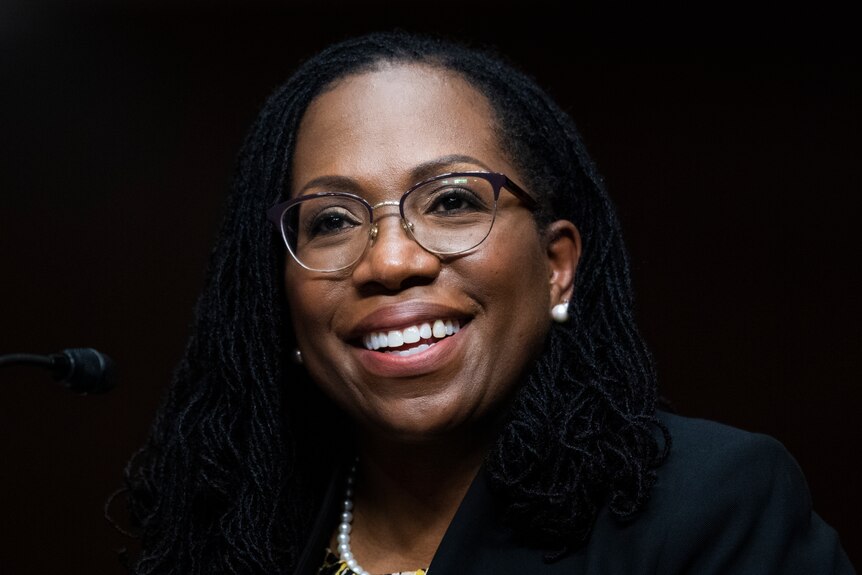 A black woman in judge's robes smiles before a microphone.