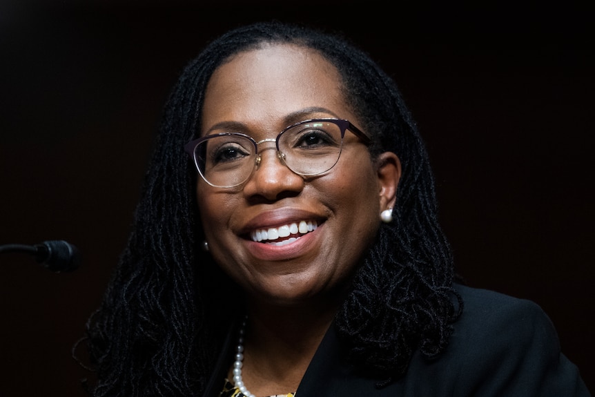 Una donna di colore in veste da giudice sorride davanti a un microfono.