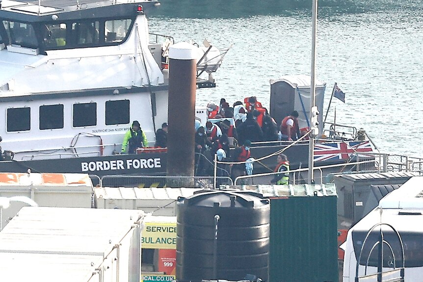 A group of people with life jackets on stand on a boat labelled 'border force' and bearing a UK flag