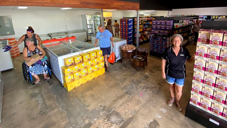 A woman stands in a supermarket setting with people shopping in the background.