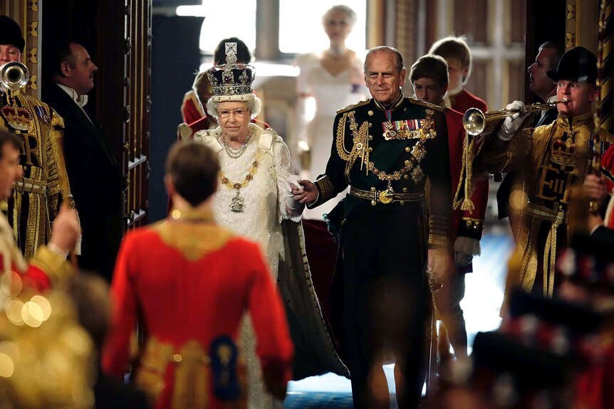 Queen Elizabeth II and Prince Philip hold hands as they walk through the Royal Gallery of the House of Lords.