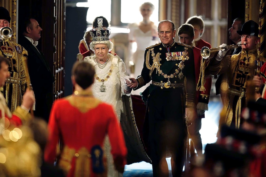 Queen Elizabeth II and Prince Philip hold hands as they walk through the Royal Gallery of the House of Lords.
