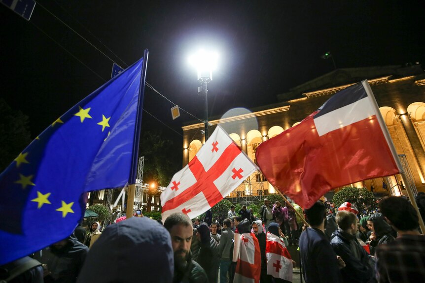 Protesters wave a Georgian and an EU flag in front of Georgia's parliament in Tbilisi