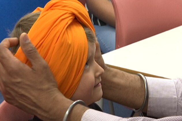 An orange turban is tied around young child's head with mans hands