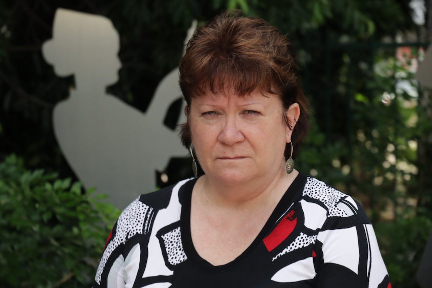 A woman with short, dark hair looks seriously at the camera.