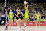 An Australian netballer gets ready to send the ball towards the net as New Zealand defenders look on.