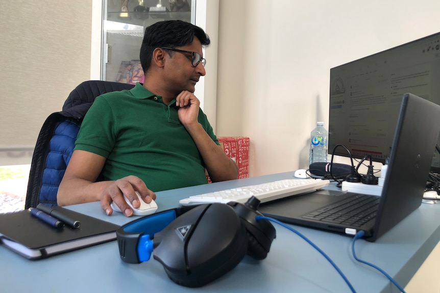 A man in a green shirt looks at a computer monitor.