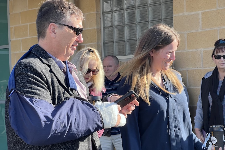 A man and a woman wearing dark clothing smile as they stand outside a court building.