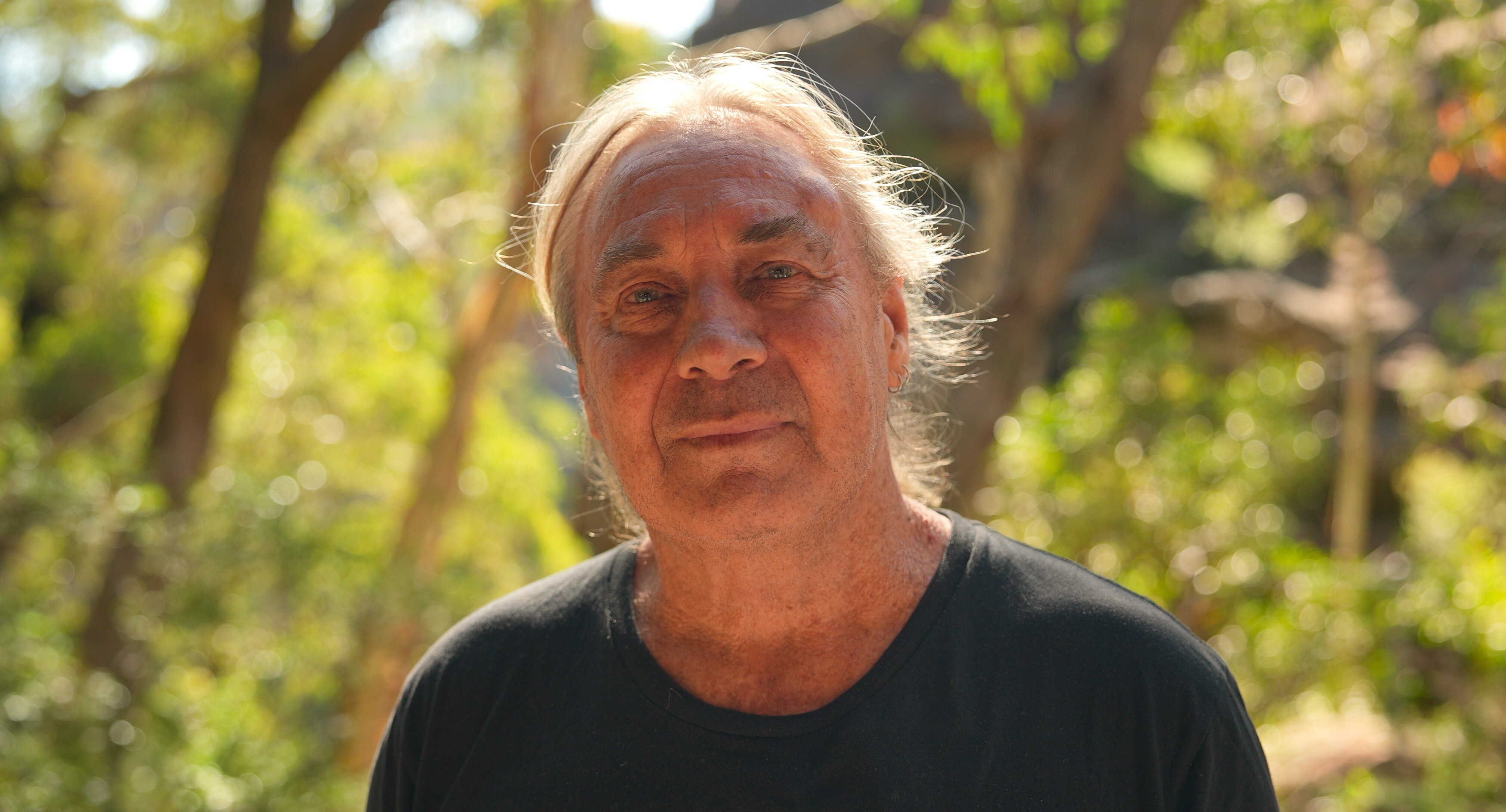 A man, smiling, standing in front of trees.