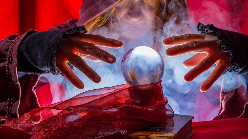 A hooded face and two hands surrounding a crystal ball with smoke