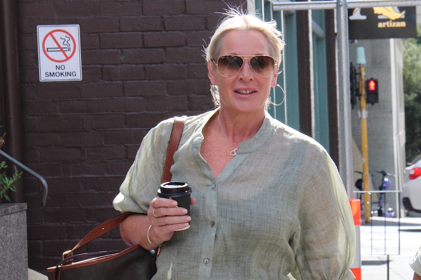 A woman walking down the street holding a coffee.